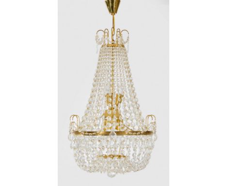 Deckenlüster im Empire-StilMessing und farbloses Glas. Balusterförmiger Korpus aus Prismenschnüren im Verlauf. Gebogte Strebe