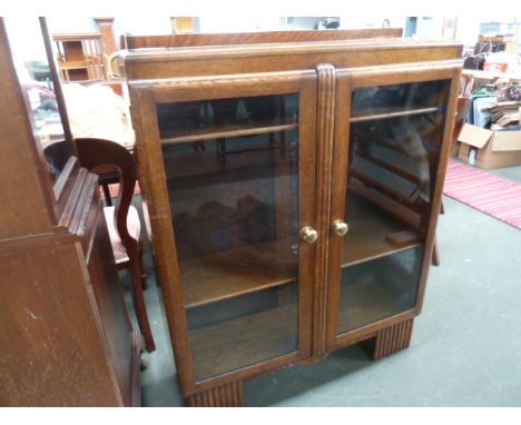 An Art Deco style oak display cabinet with glazed doors and three internal shelves, brass handles, over block feet 90cmW x 11