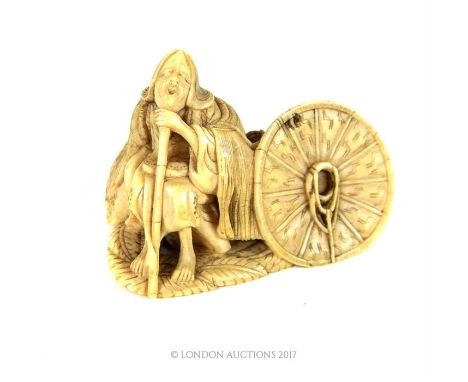 A late 18th / early 19th century Japanese netsuke in the form of a seated sibyl with a large hat, probably carved from the to