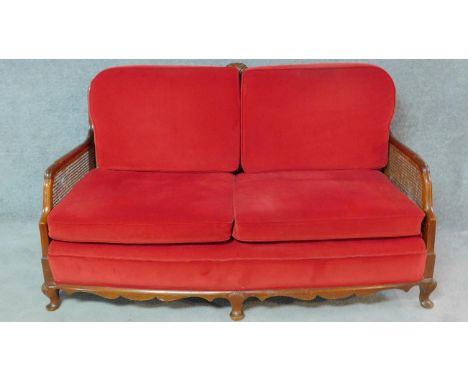 A mid 20th century walnut framed bergere sofa with caned panelled back and sides in red upholstery on shell carved cabriole s