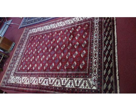 A Northeast Persian Turkoman carpet, bearing repeating Tekkeh motifs on a terracotta field, guarded by multi geometric border