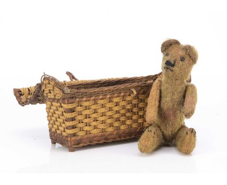 A teddy bear in a basket 1910-20, with short golden mohair, black boot button eyes, pronounced muzzle, black stitched nose an