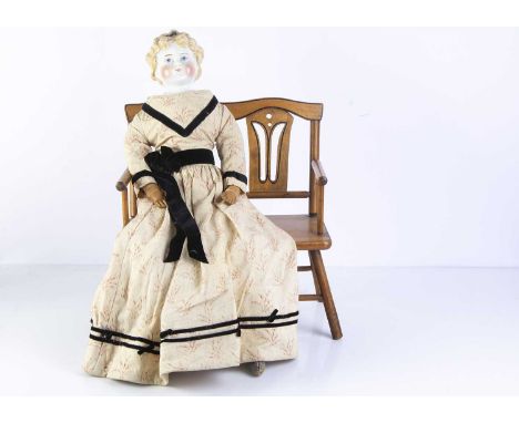 A 19th century German china shoulder head doll, with blonde painted and moulded curly hair held by a black ribbon around her 