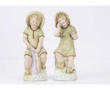 A small pair of Gebruder Heubach children by the seaside, with intaglio eyes, blonde painted hair, the clothes  shades of gre