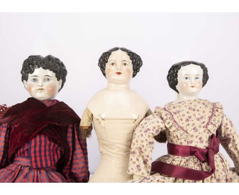 Three china shoulder-head dolls,  two late 19th century with black painted and moulded hair, stuffed bodies and dressed —24 1