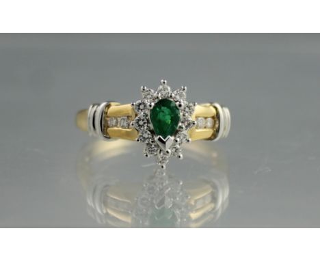 14CT GOLD EMERALD AND DIAMOND RING.  The pear shaped emerald surrounded by twelve diamonds and having two diamonds and a trip