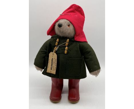 A Gabrielle Designs Paddington Bear in red Dunlop boots, green coat and red hat with tag.