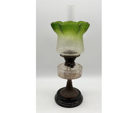 An antique oil lamp with frilled edged green glass shade