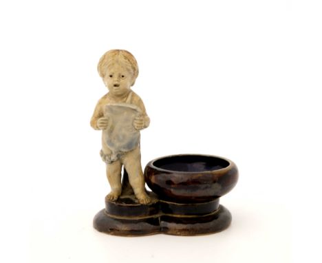 George Tinworth for Doulton Lambeth, a stoneware figural salt cellar, modelled as a chorister putto, with garland sash and sh