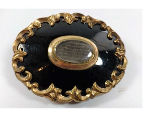 A Victorian Memorial brooch in black enamel and gold coloured metal, with a framed lock of hair to centre. provenance 80 Rose