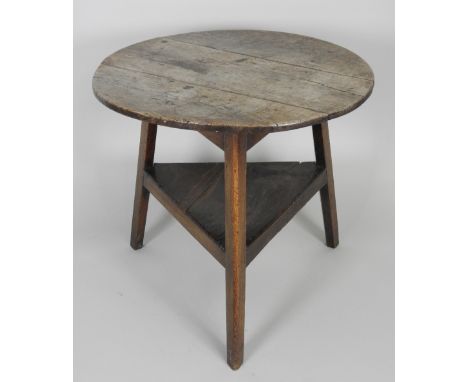 A George III oak and elm cricket table the circular three plank top on chamfered out-swept legs united by a shelf stretcher, 