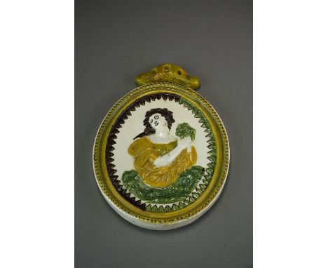 An early 19th century oval Prattware plaque decorated in relief with a brunette maiden holding a green laurel within a brown 