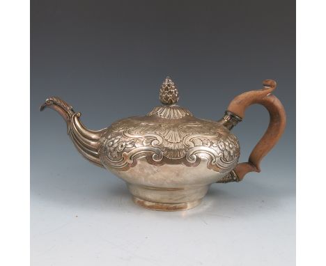 A Georgian silver tea pot, with bud finial, the body embossed with flowers and scrolls, engraved with a crest, London 1812, m