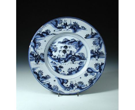 An 18th century Dutch Delftware blue and white charger, decorated in the chinoiserie manner with figures seated amongst rockw