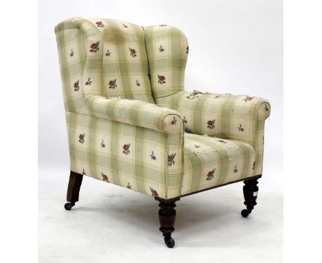 AN EDWARDIAN UPHOLSTERED WING BACK ARMCHAIR with mahogany legs, terminating in brass and ceramic casters, stamped WB to one l