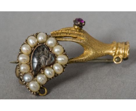 A Georgian unmarked gold ruby and seed pearl brooch
Formed as a hand holding a hair plait centred heart.  2.75 cm wide.  COND