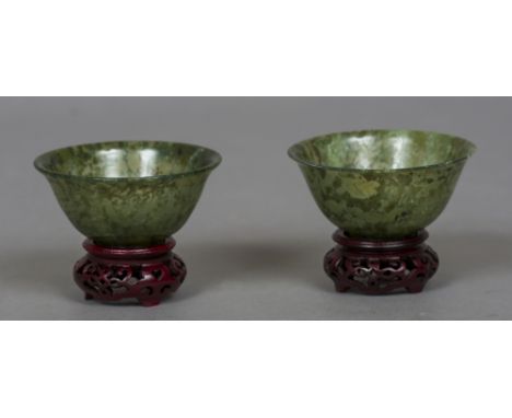 A pair of Chinese carved spinach jade bowls
Each with a flared rim and a small foot, standing on pierced carved wooden stands