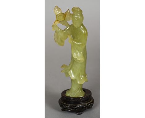 A Chinese carved jade figure of Guanyin
Modelled in flowing robes holding a flower, standing on a carved wooden plinth base. 