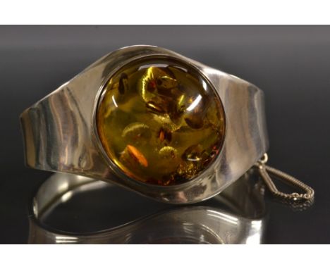 A lady's silver amber mounted hinge bangle, offset shaped top inset with a large amber cabochon, stamped 925,6.5cm wide, 36g 