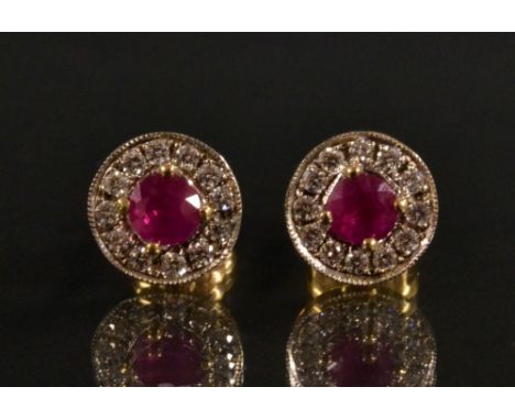 A pair of ruby and diamond cluster earrings, each with a central red ruby surrounded by a band of twelve round cut diamonds, 