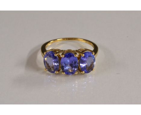 A tanzanite trilogy ring, uniform colour oval stones,quarter claw set, 18ct gold shank, stamped 750, size N/O, Birmingham 201