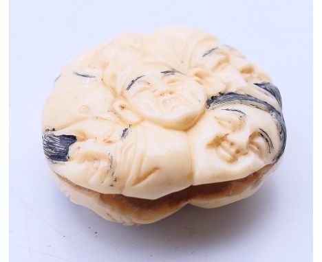 A bone netsuke depicting faces. 4 cm diameter.