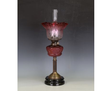 An early 20th century brass and cranberry glass oil lamp with foliate etched glass shade above a gilt metal burner, foliate m