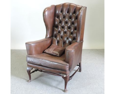 A brown upholstered button back wing armchair, on cabriole legs