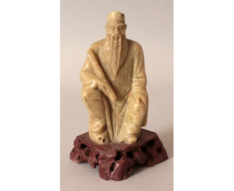 AN EARLY 20TH CENTURY CHINESE CARVED SOAPSTONE FIGURE OF A SCHOLAR, seated on a rocky plinth and bearing a scroll, 5.7in high