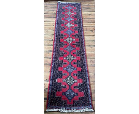 A Persian Senneh runner, having a row of central medallions, on a red ground315 x 80cm