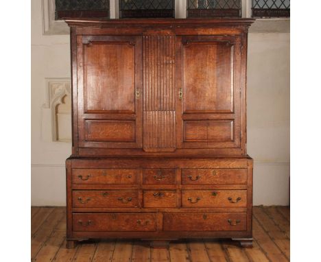 A George III oak housekeeper's cupboard, of large proportions, the panelled doors flanking a fluted panel above an arrangemen
