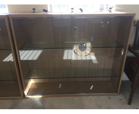 A beech effect wall mountable display cabinet with sliding glass panel front. With 2 internal glass shelves and lighting. Mea