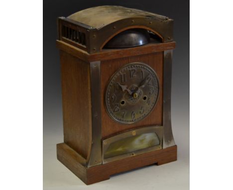 An Arts and Crafts oak mantle clock, the arched top above brass dial with stylized numerals, twin winding holes, above slende