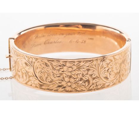A 9ct gold bangle, with floral and foliate engraved decoration to front panel, hinged, push-in clasp with safety chain, UK ha