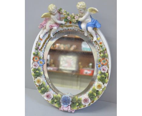 A flower encrusted porcelain mirror decorated with cherubs 