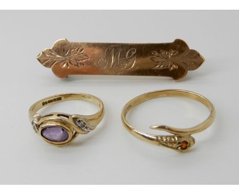 A 9ct gold garnet set snake ring size P1/2, a 9ct amethyst and diamond accent ring size G1/2, and a K9 brooch weight combined