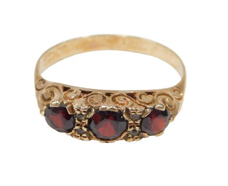 A three stone garnet dress ring, set with three round brilliant cut garnets and two tiny diamonds, on scroll design shoulders