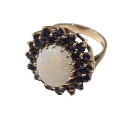 A 9ct gold opal and sapphire dress ring, of chunk design, the central opal 5.4mm x 2.4mm, surrounded by layers of sapphires, 