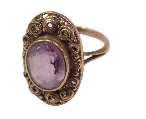 A 9ct gold amethyst dress ring, the oval amethyst in rub over setting, with oval shield with raised scroll design and V splay