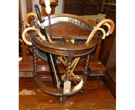 An early 20th century beaded oak demi lune twin division stick stand on barley twist turned supports with sundry walking stic