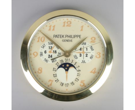 A Patek Philippe watch style wall clock, featuring a gold bezel and gold dial featuring Arabic Numeral markers.
