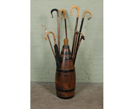 A wood and metal bound barrel/pitcher converted to a stick stand, housing an assortment of walking sticks and umbrella.