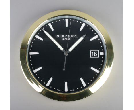 A Patek Philippe watch style wall clock, featuring a gold bezel and black dial featuring baton markers and artificial date wi