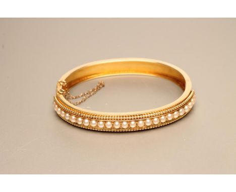 AN EDWARDIAN STIFF HINGED BANGLE, the upper section set with twenty five (split?) pearls to an applied rope twist border, wit