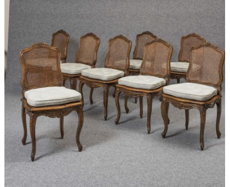 A SET OF EIGHT LOUIS XV STYLE CARVED WALNUT DINING CHAIRS, c.1900, the channelled frame with shield back with arched flower c