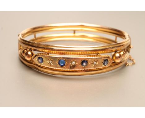 AN EDWARDIAN 9CT GOLD STIFF HINGED HOLLOW BANGLE of open form, the upper section centred by a panel gypsy set with four sapph
