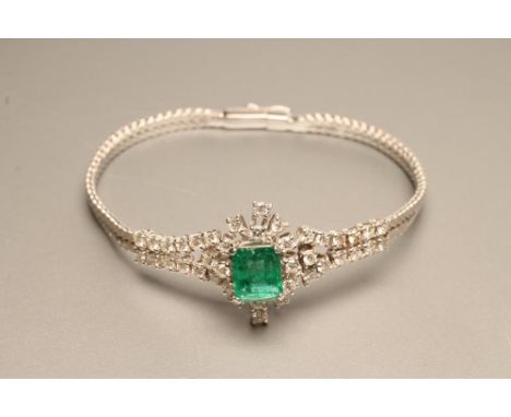 AN EMERALD AND DIAMOND BANGLE, the square cut emerald claw set to an open border of fourteen round brilliant cut diamonds to 