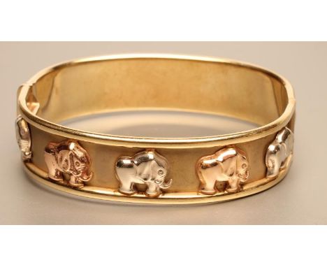 AN ITALIAN TRI-COLOUR 9CT GOLD STIFF HINGED HOLLOW BANGLE, stamped and applied with a train of ten elephants, with safety cat
