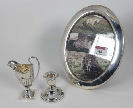 An Elizabeth II oval silver photograph frame Sheffield 1987, sight 18x13cm, together with a dwarf silver candlestick loaded, 