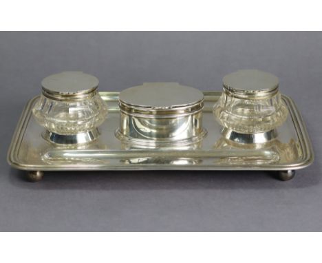 A George V silver large desk inkstand of rectangular shape with raised moulded rim, a pen trough either side, an oval straigh